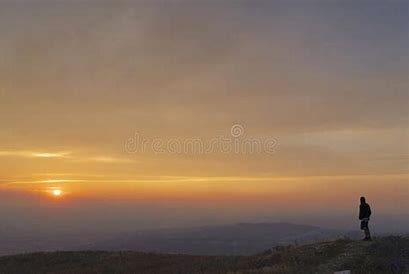 man standing on mountain looking at sunset